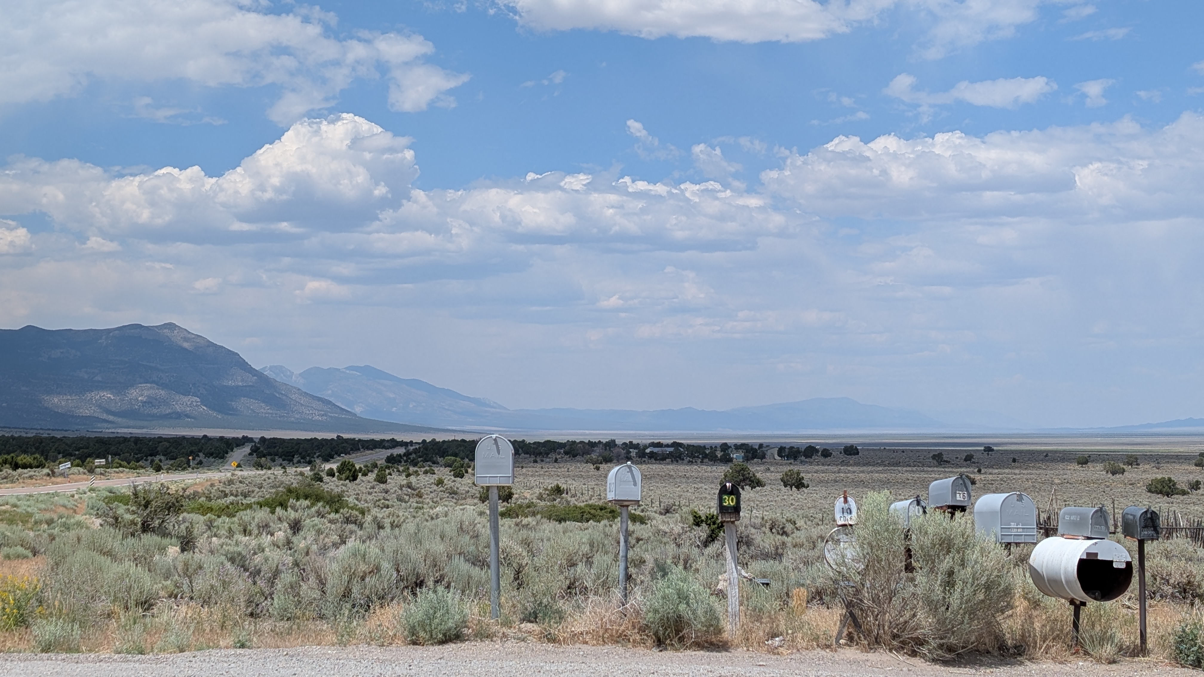 Mailboxes by a desert road, mountains and clouds beyond